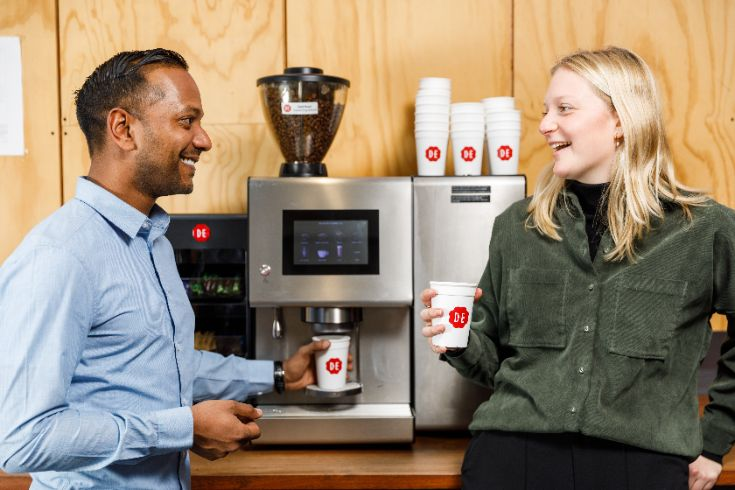 two people talking and enjoying coffee in front of the coffee machine