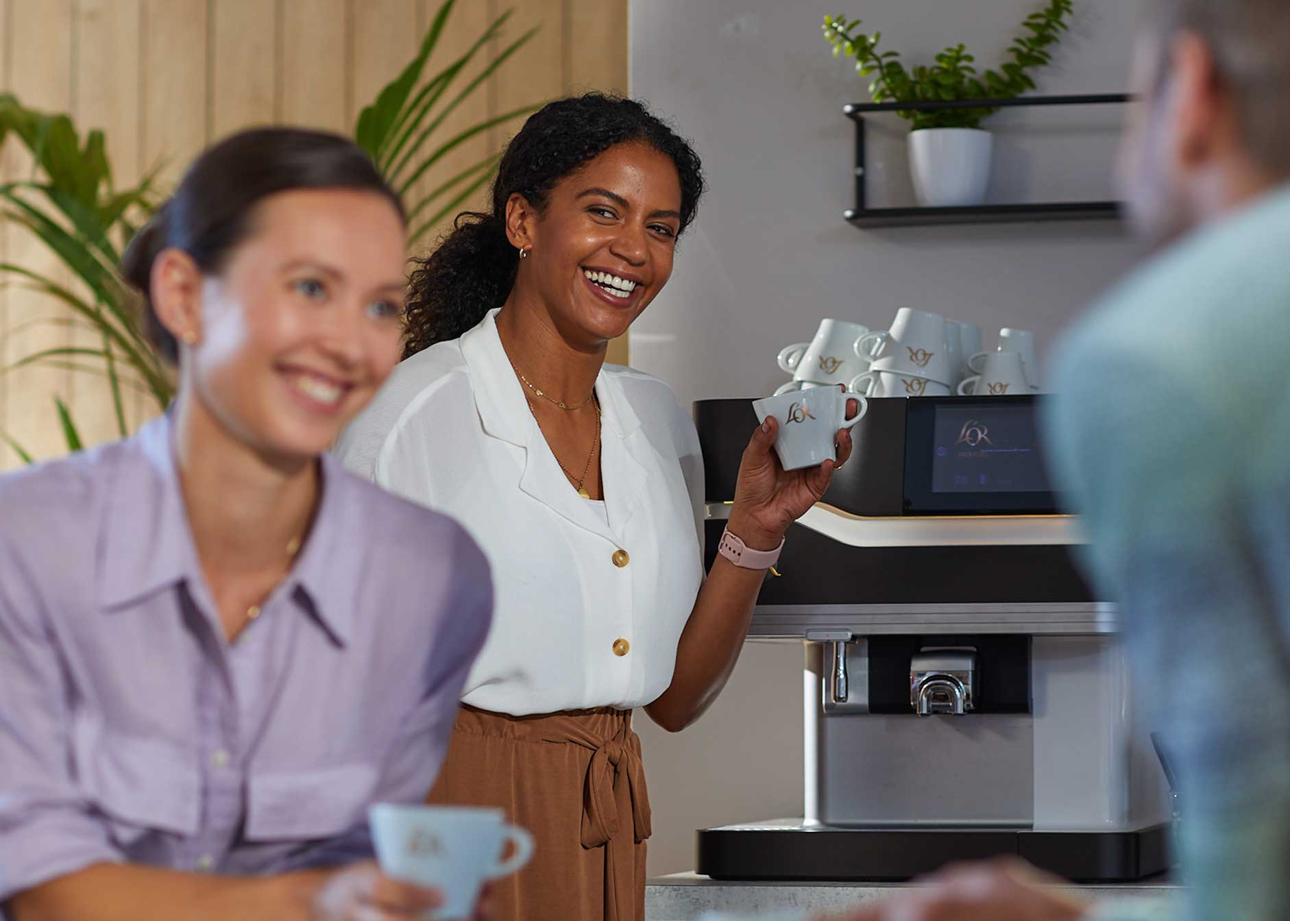 Trois personnes discutent autour d’une machine à café, chacune tenant une tasse.